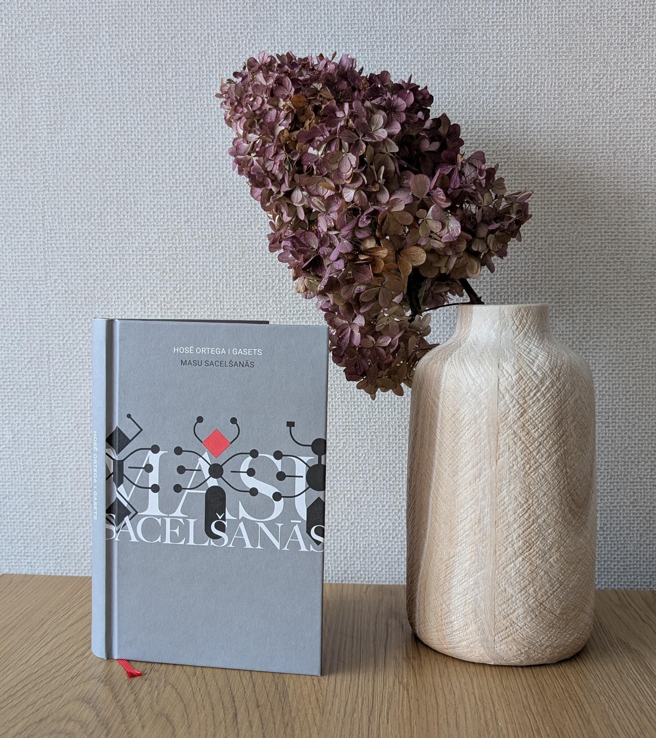 Uz galda stāvus nolikta grāmata Hosē Ortega i Gasets "Masu sacelšanās". Blakus lielā vāzē izkaltēts hortenzijas zars.