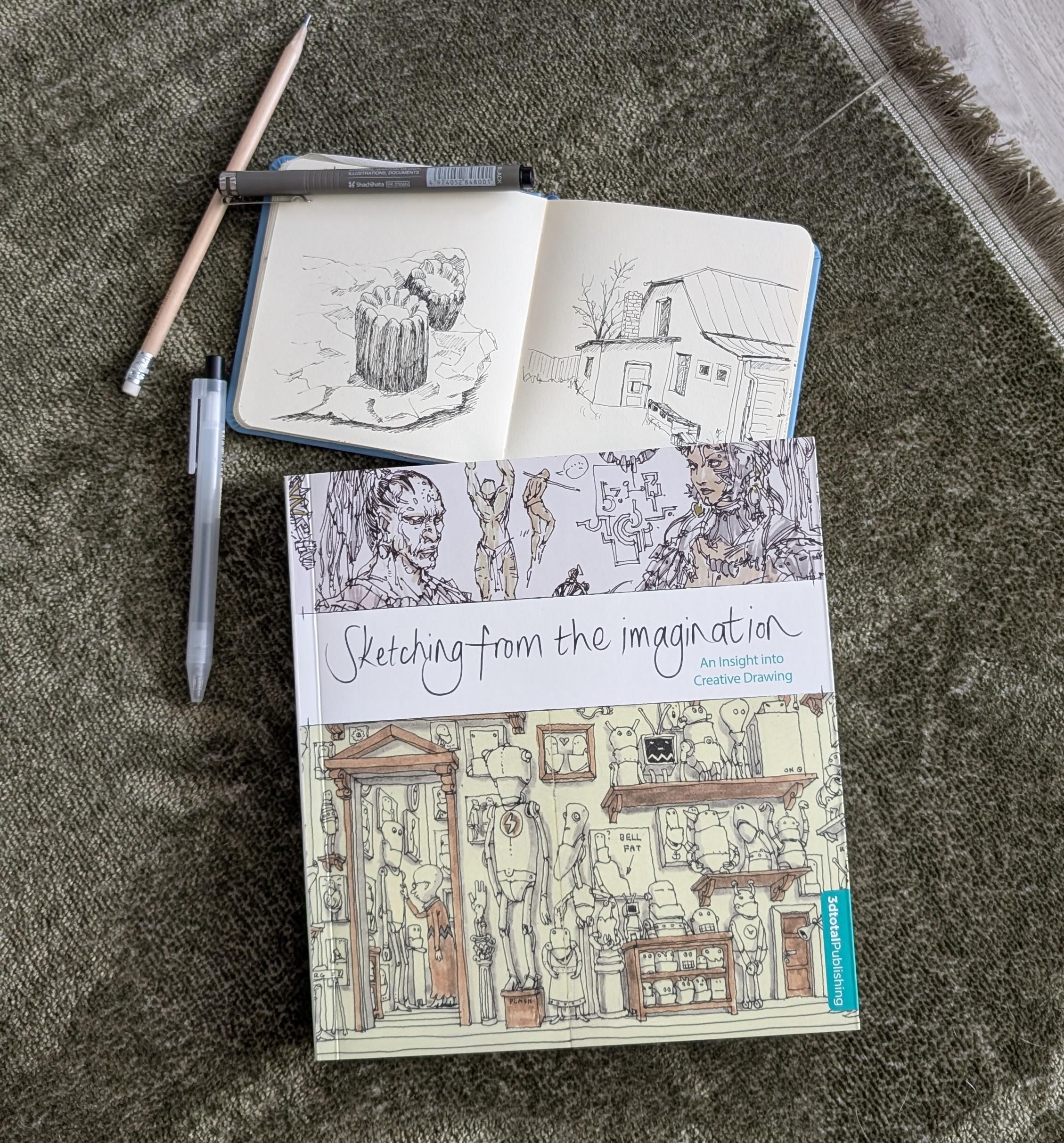 Grāmata "Sketching from the imagination" nolikta uz paklāja. Blakus pildspalvas, zīmulis un atvērta skiču klade.